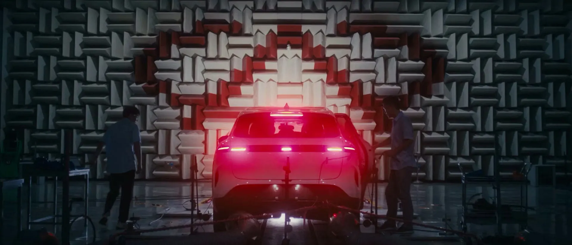 Chery engineers testing a car in an acoustic test chamber, its rear lights glowing red against the sound-absorbing wall